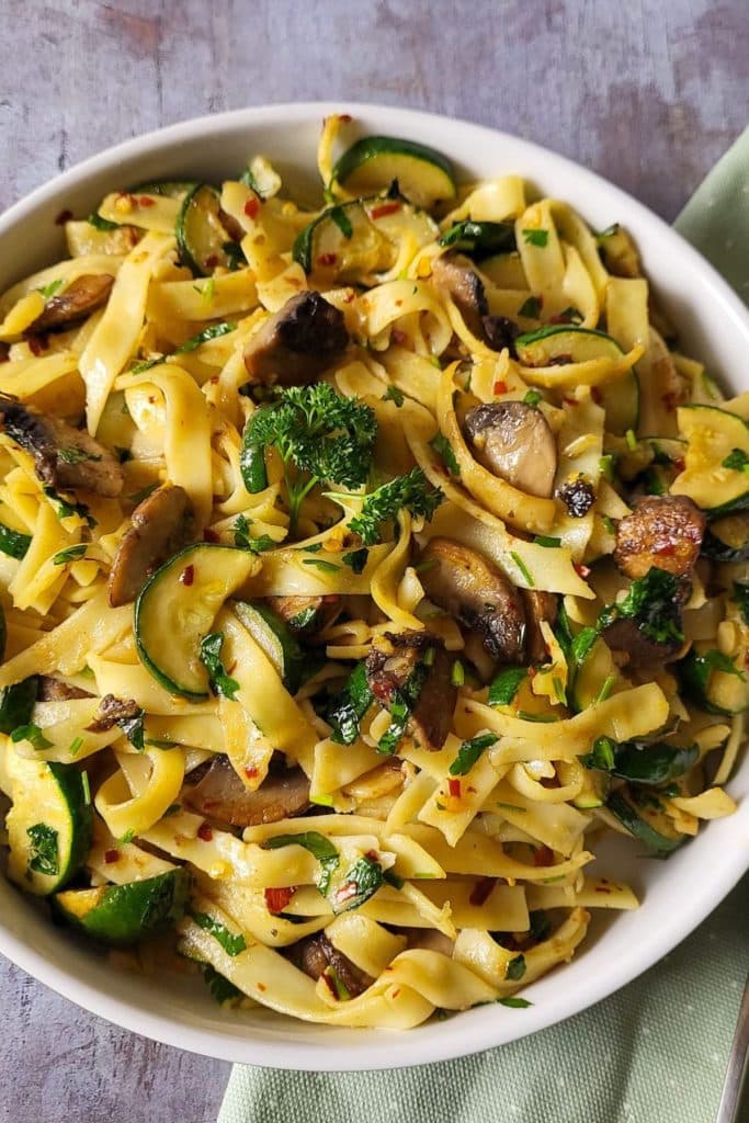 A close-up zucchini and mushroom pasta in white dish.