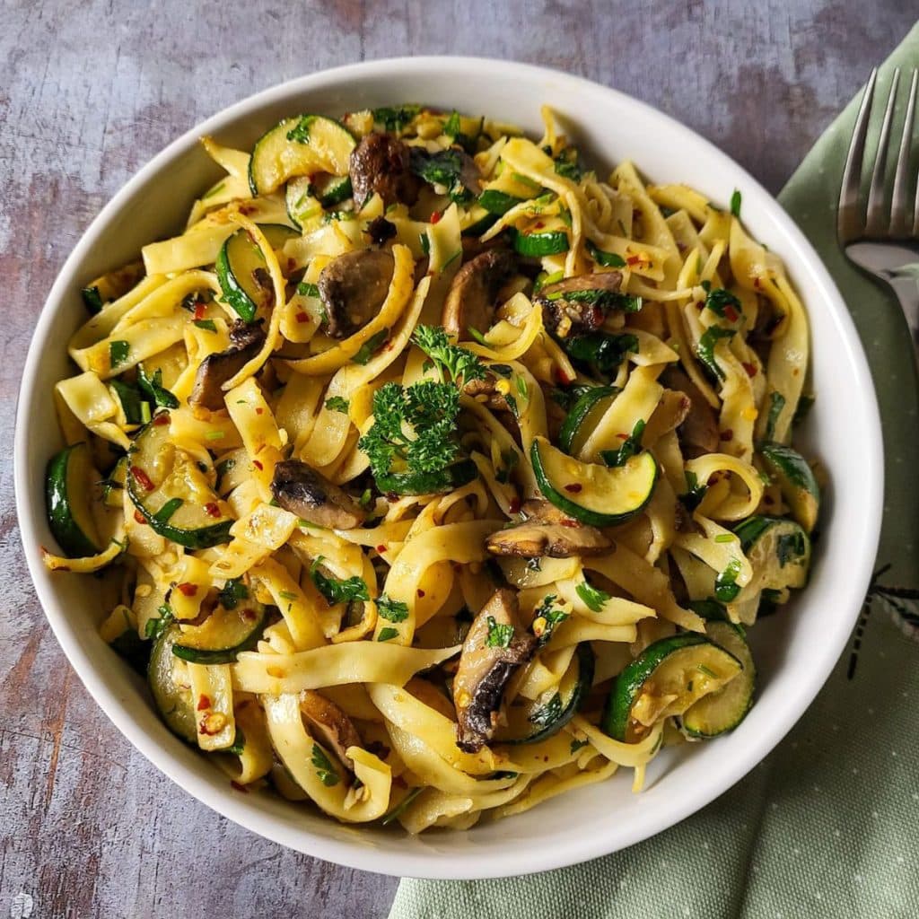 Zucchini mushroom pasta with mint green napkin in the background.