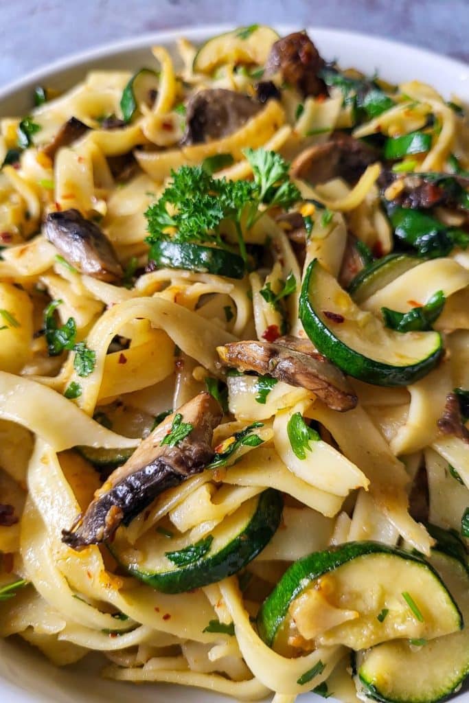 Tagliatelle pasta with mushrooms and zucchini garnished with parsley.