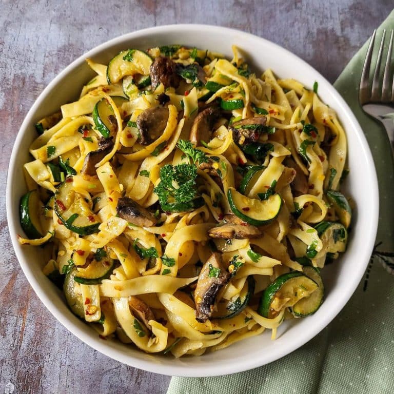 Zucchini mushroom pasta with mint green napkin in the background.