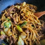Beef udon noodles stir fry with pak choi in a wok.