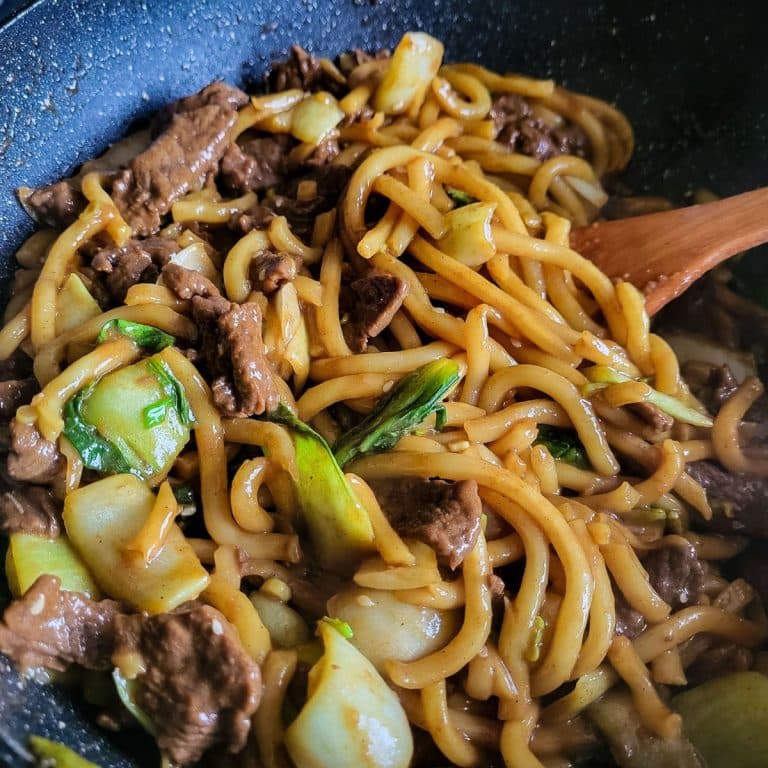 Beef udon noodles stir fry with pak choi in a wok.