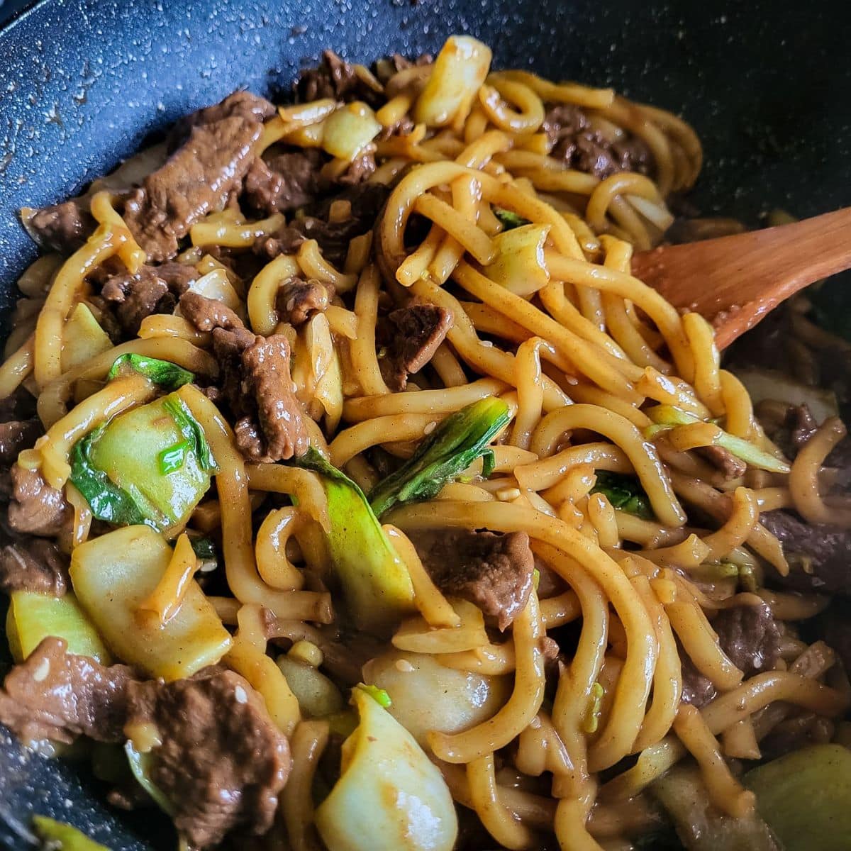Beef udon noodles stir fry with pak choi in a wok.